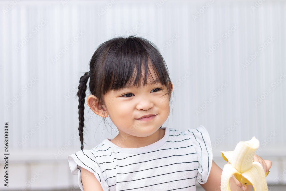 Portrait image of baby 3-4 years old. Happy Asian child girl enjoy eating a banana with sweet smiling. Food and healthy kids concept. Portrait image of baby 3-4 years old. Happy Asian child girl enjoy eating a banana with sweet smiling. Food and healthy kids concept.