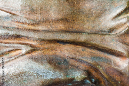 Close-up photo texture of worn and aged copper or bronze statue material with horizontal folds.