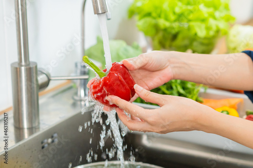 Close up asian young housekeeper woman,  washing sweet pepper, red paprika, vegetables with splash water in basin of water on sink in kitchen, preparing fresh salad, cooking meal. Healthy food people.