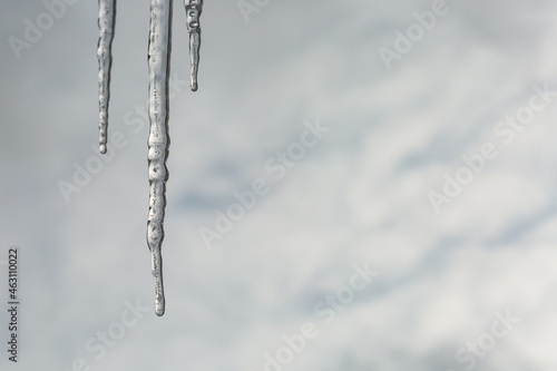 Three icicles hanging against cloudy sky background © karelian
