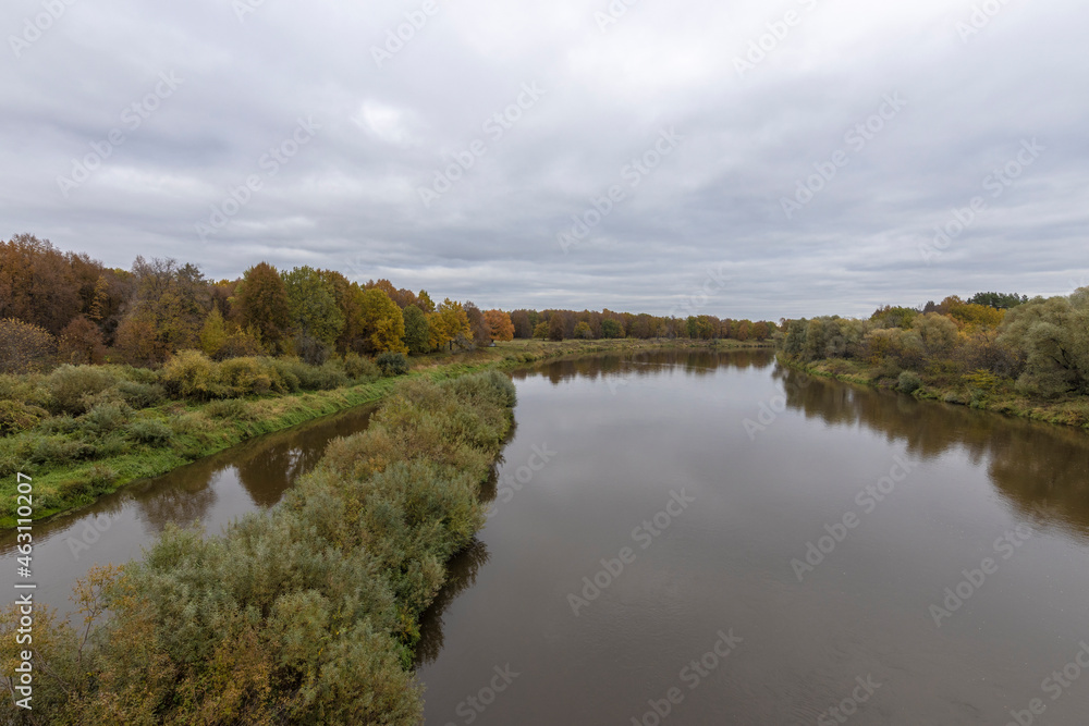 Autumn landscape with a river. Cloudy autumn day by the river. View of the river with trees and bushes on the bank. Bright colors of autumn on a cloudy day. Autumn landscape with a river. Cloudy autumn day by the river. View of the river with trees and bushes on the bank. Bright colors of autumn on a cloudy day.