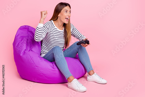 Full length photo of young hooray brown hairdo lady sit playstation wear shirt jeans shoes isolated on pink background