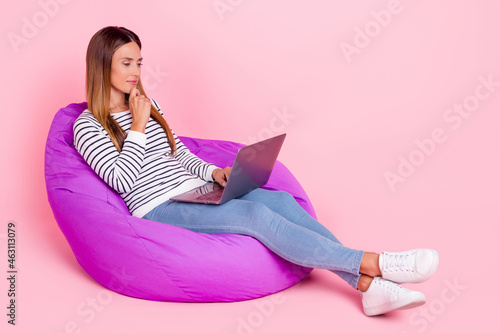 Photo of thoughtful charming mature lady wear striped sweater sitting beanbag arm chin working modern gadget isolated pink color background