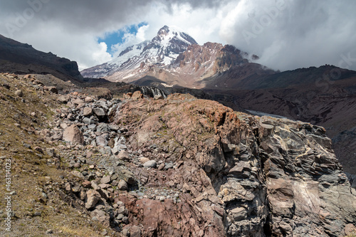 A strong overcast building up above Mount Kazbeg in Caucasus, Georgia. Rainy clouds. There slopes are barren and stony below the snow-capped peak and the Gergeti Glacier. Massive glacier foot