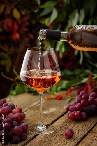 Autumn cozy romantic evening outdoors, wooden table with glass with rose wine, rose wine is poured from the bottle into the glass