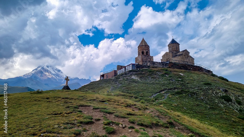 A view on Gergeti Trinity Church in Stepansminda, Georgia. The church is located on a high Caucasian mountain. Clear and blue sky above the church. In the back there are high mountain chains.