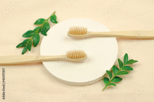 Eco-friendly personal hygiene items. Two wooden toothbrushes and green leaves on a round podium. No waste  no plastic