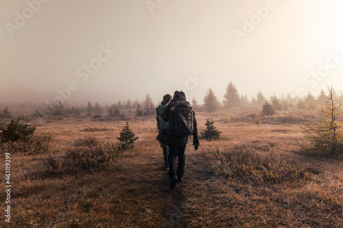 Man hiker with backpack walking in foggy meadow on autumn