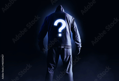 Fototapeta Naklejka Na Ścianę i Meble -  Photo of scary horror stranger stalker man in black hood and clothing on dark background with glowing question symbol on his back.