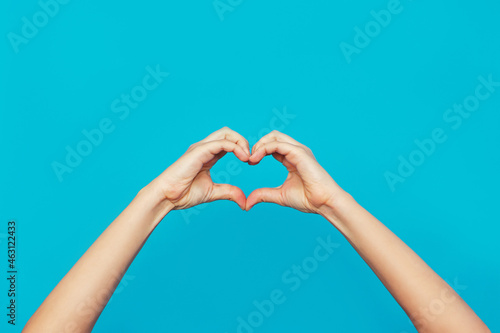 Female hands showing a heart shape isolated on a bright color blue background. Sign of love  harmony  gratitude  charity. Feelings and emotions concept