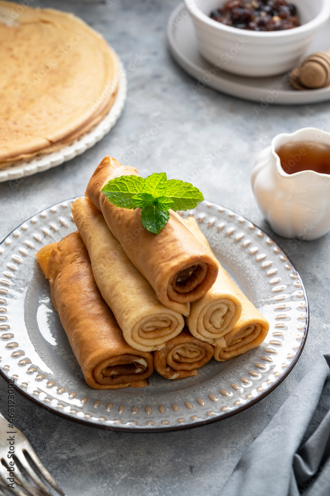 Rolled crepes or thin pancakes, served with jam and honey, on grey background. Rolled crepes or thin pancakes, served with jam and honey, on grey background.
