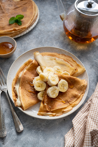 Crepes or thin pancakes, served with honey and cup of tea, on grey background.