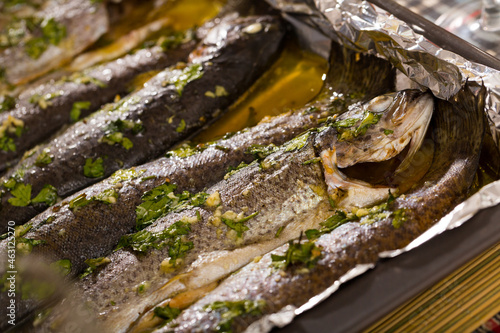 Appetizing baked whole trout seasoned with garlic and greens served in oil on baking tray