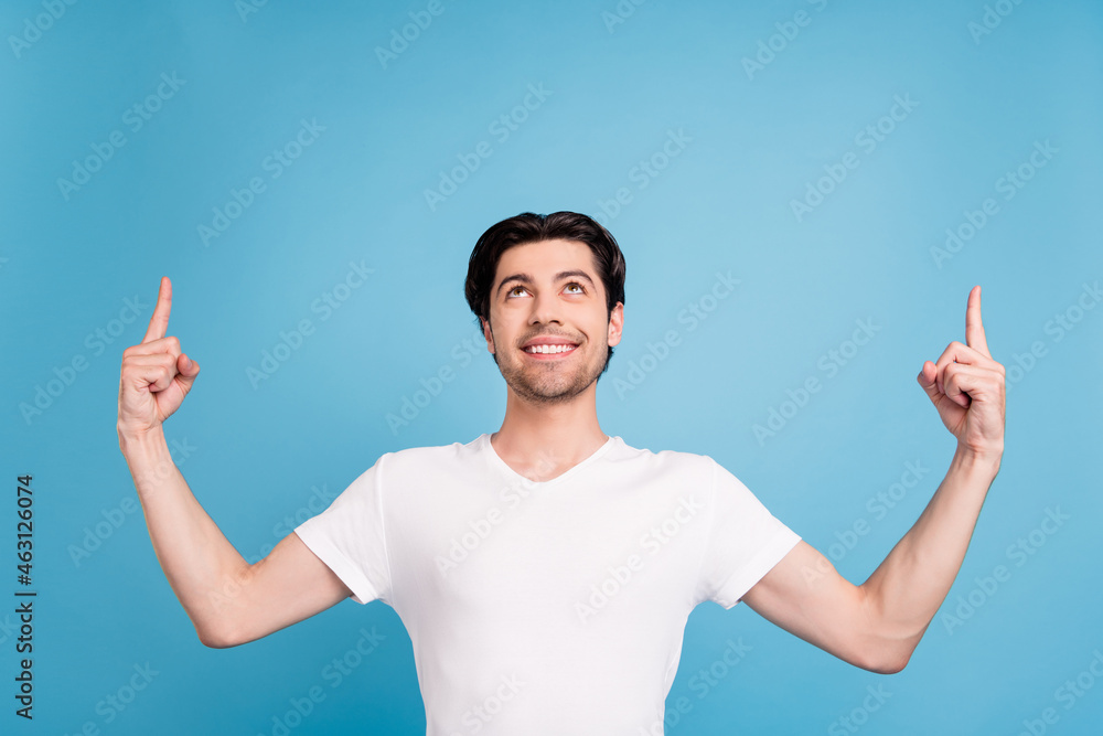 Photo of dreamy reliable guy indicate fingers empty space look up wear white t-shirt isolated blue color background Photo of dreamy reliable guy indicate fingers empty space look up wear white t-shirt isolated blue color background