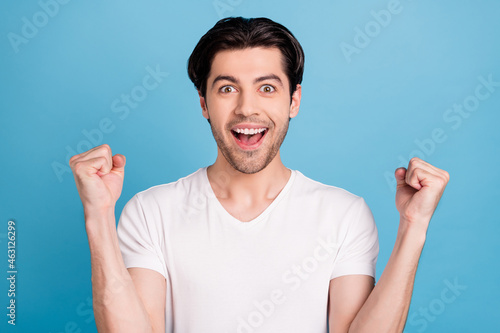 Photo of champion guy raise fists celebrate victory raise fists wear white t-shirt isolated blue color background