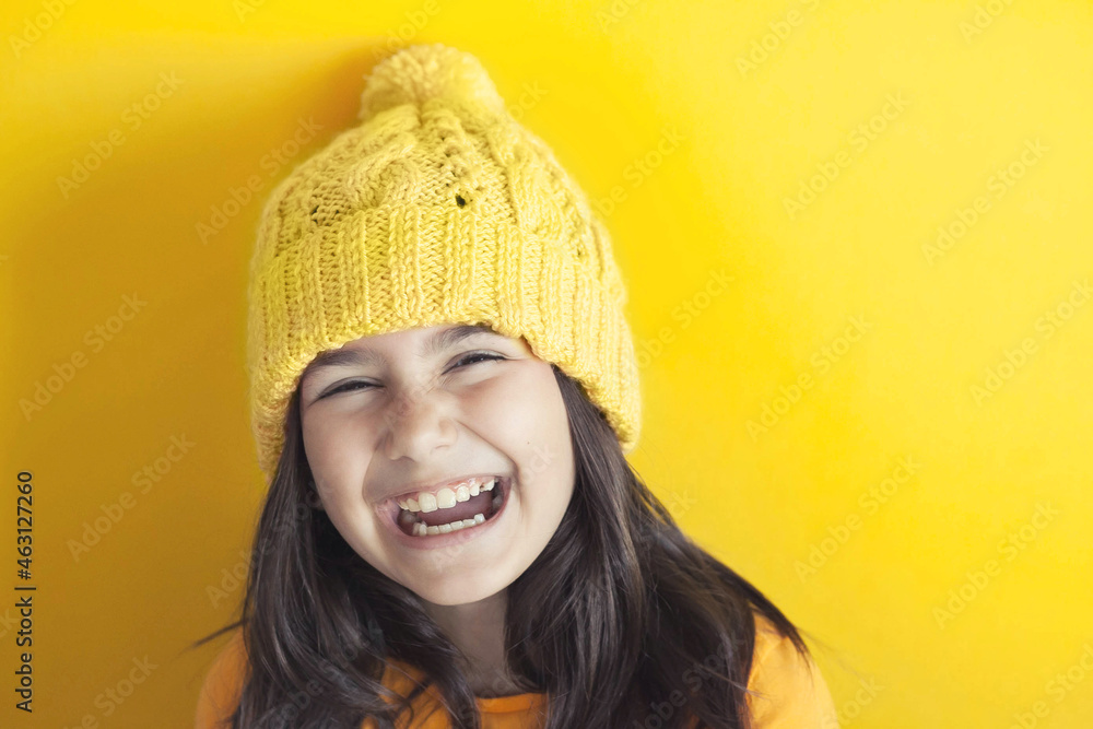 Happy beautiful smiling child girl in knitted hat on yellow background Space for text. Yellow colour consept. Spase for text.