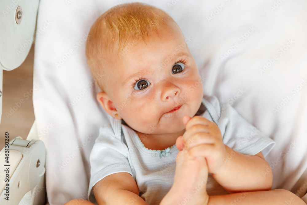 Cute little newborn girl with smiling face looking at camera on white background. Infant baby resting playing lying down on feeding chair at home. Motherhood happy child concept. Cute little newborn girl with smiling face looking at camera on white background. Infant baby resting playing lying down on feeding chair at home. Motherhood happy child concept.