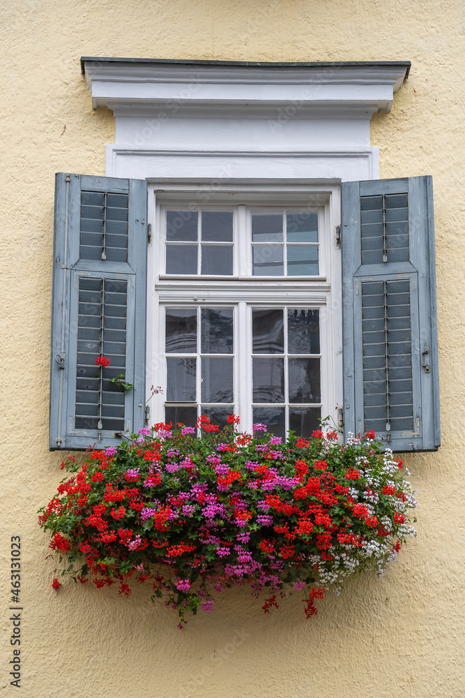 Beige plaster facade of a mountain house and windows with colorful flowers in Austria