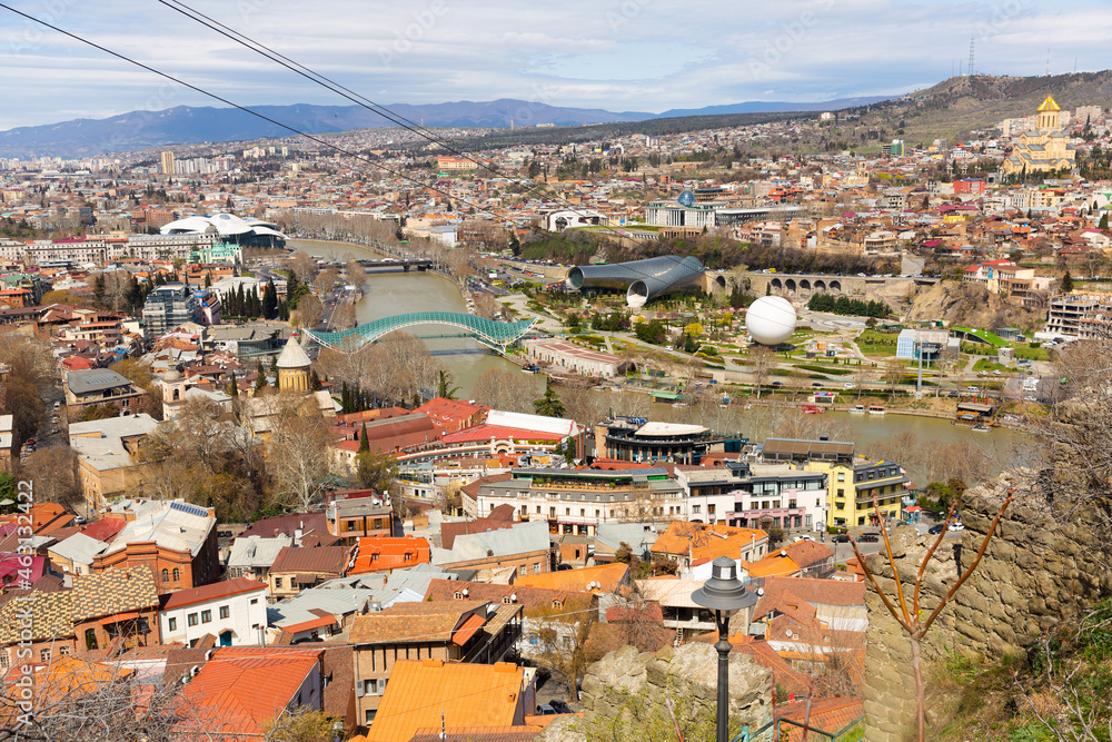 Scenic view of Tbilisi Old town on banks of Kura river on sunny spring day overlooking modern pedestrian Bridge of Peace, Music Theater building and air balloon in Rike Park, Georgia