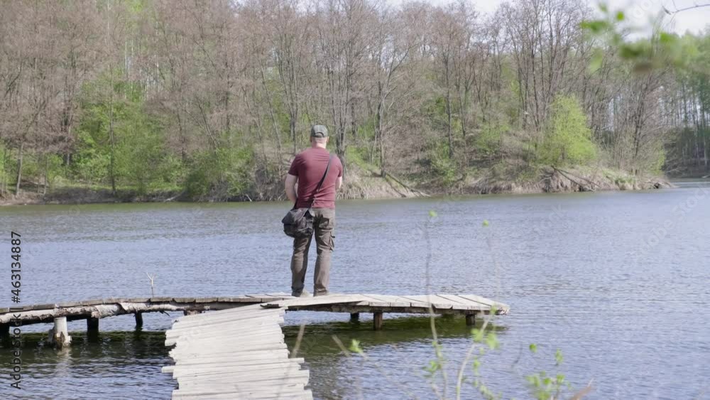 Wide shot fisherman catches fish while standing on a wooden bridge. Adult man with fishing rod Wide shot fisherman catches fish while standing on a wooden bridge. Adult man with fishing rod