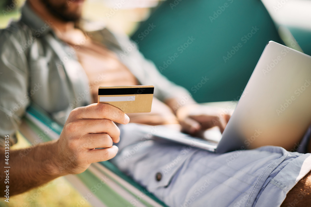 Fototapeta premium Close-up of man uses credit card and laptop while e-banking in nature.