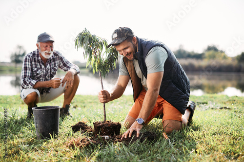 Photo Happy man plants tree sapling with his father by the lake.
