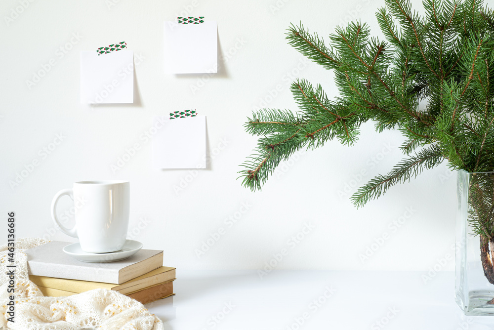 Festive breakfast still life.Cup of coffee, books and vase with fir branches.Empty notepads mockup hanging on the white wall.Christmas decor.Working space, home office.Happy new year resolutions, list Festive breakfast still life.Cup of coffee, books and vase with fir branches.Empty notepads mockup hanging on the white wall.Christmas decor.Working space, home office.Happy new year resolutions, list