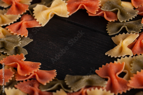 Dry farfalle tricolore pasta pattern. Uncooked Macaroni. Heap of raw traditional italian pasta on a wooden table with copyspace.