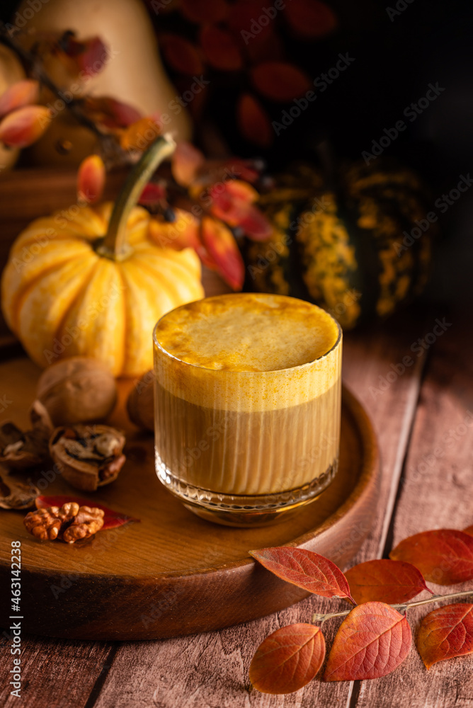 Pumpkin spicy latte in a stylish glass on a dark background with pumpkins and autumn leaves. Autumn composition in warm colors Pumpkin spicy latte in a stylish glass on a dark background with pumpkins and autumn leaves. Autumn composition in warm colors