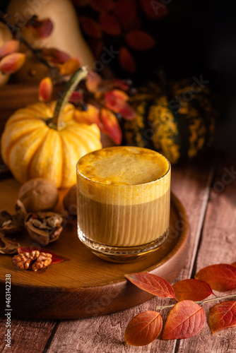 Pumpkin spicy latte in a stylish glass on a dark background with pumpkins and autumn leaves. Autumn composition in warm colors