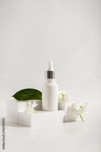 Composition of a white glass dropper bottle with a skin care product and white flowers on a white background. Health and beauty concept. Organic natural cosmetics.