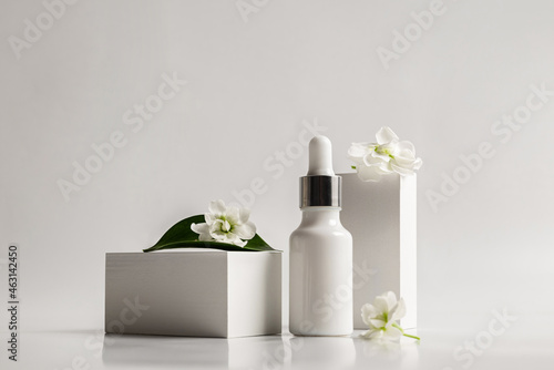 Composition of a white glass dropper bottle with a skin care product and white flowers on a white background. Health and beauty concept. Organic natural cosmetics.