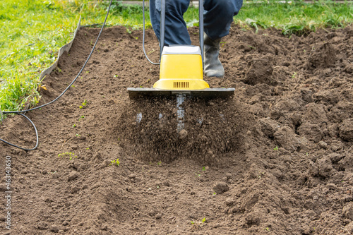Loosening the soil in the garden beds with an electric hand-held cultivator photo
