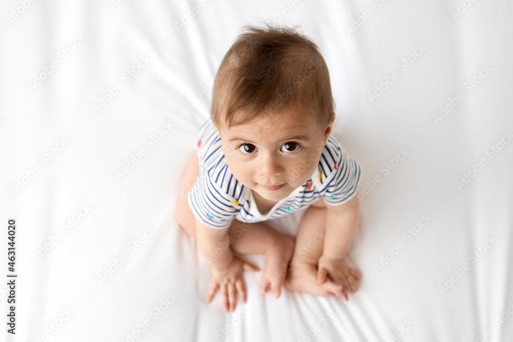 Top view of cute baby sitting on white bed looking up Top view of cute baby sitting on white bed looking up