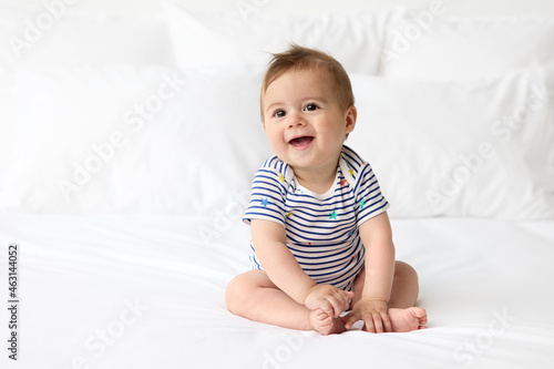 Cute smiling baby sitting on white bed photo