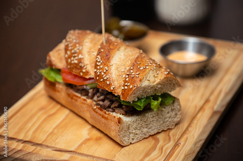 Baguette de carne asada con aderezo sobre una tabla de madera