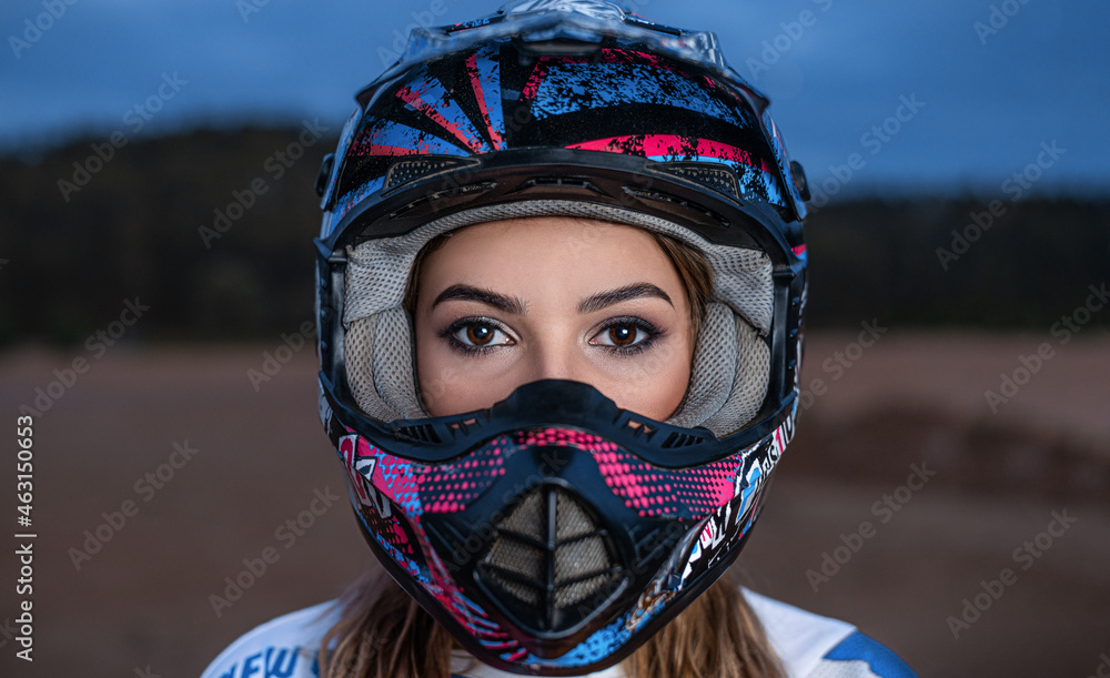 a beautiful girl with big eyes in a helmet looks at the camera against a background of blue sky, forest and sand