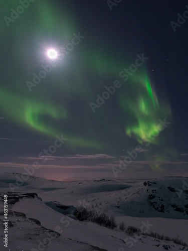 In winter  the moon and the aurora borealis are in the sky.