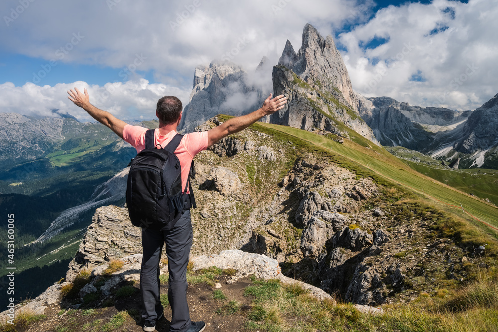 A man with backpack raised his hands enjoying landscape of Seceda peak in Dolomites Alps, Odle mountain range, South Tyrol, Italy, Europe. Travel vacation concept