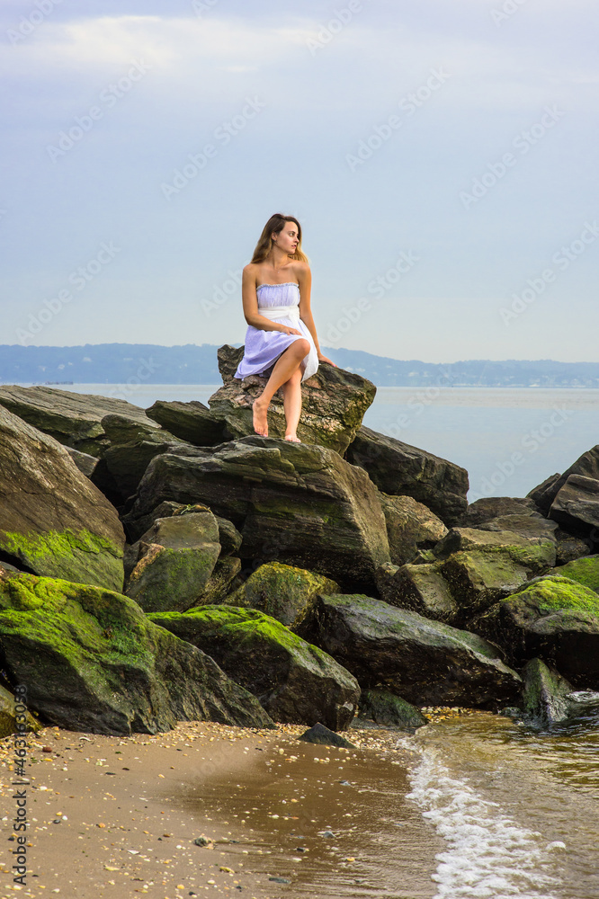 In the evening, a pretty girl is siting on rocks on the beach, waiting for you.