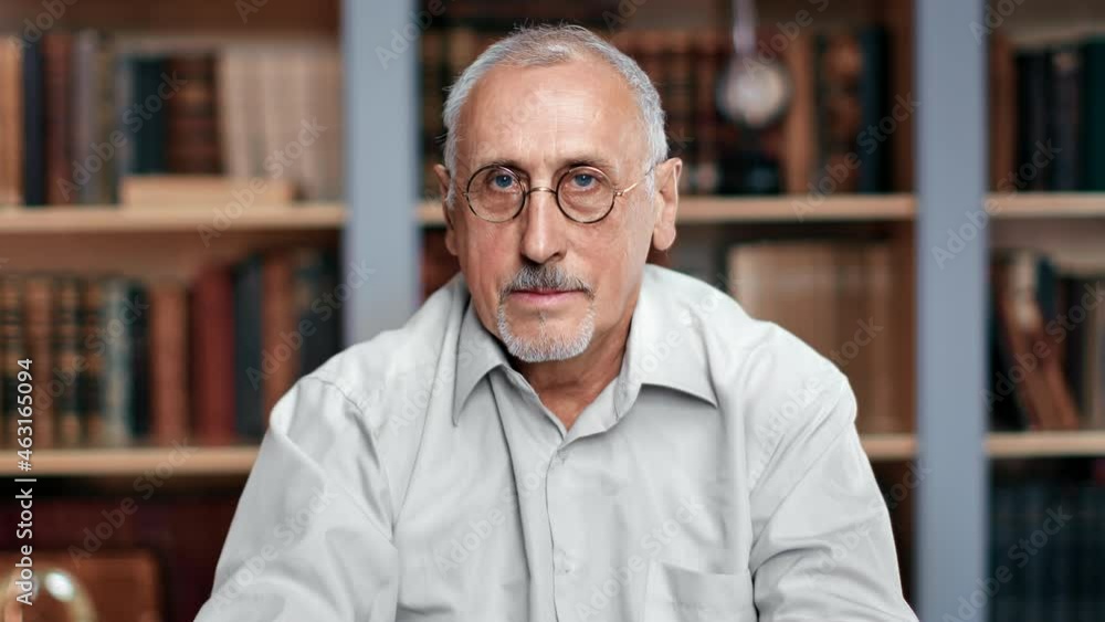 Portrait of pensive gray haired grandfather in eyeglasses posing at home library living room Portrait of pensive gray haired grandfather in eyeglasses posing at home library living room