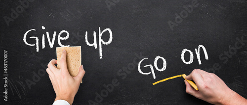 hand with sponge redy to remove the message GIVE UP and another with chalk writing the message GO ON on a chalkboard