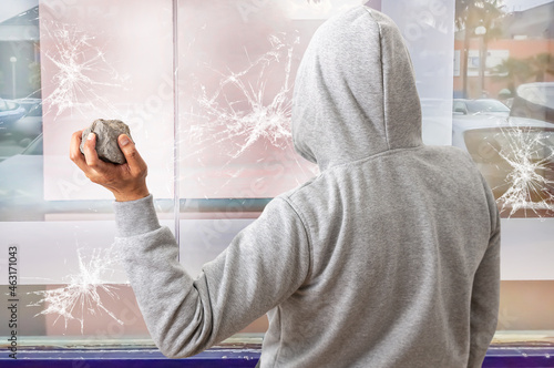 Rear view of a man holding a stone to throw it against a glass and break a window.