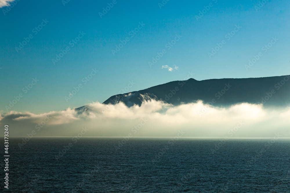 Early morning in the sea bay against the background of mountains, blue sky and fog in the distance rising above the water.