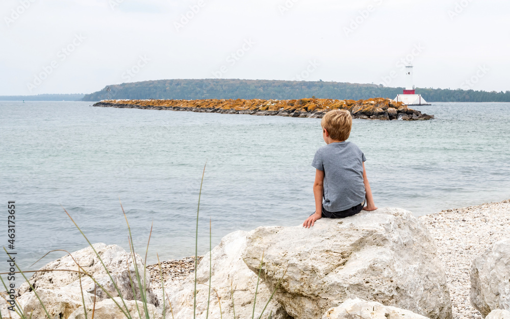A young kid is sitting on a rock to enjoy a quiet day