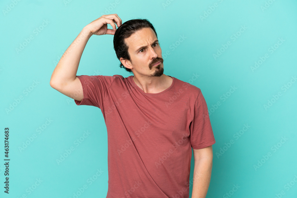 Young caucasian man isolated on blue background having doubts while scratching head Young caucasian man isolated on blue background having doubts while scratching head