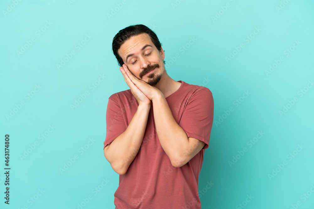 Young caucasian man isolated on blue background making sleep gesture in dorable expression Young caucasian man isolated on blue background making sleep gesture in dorable expression