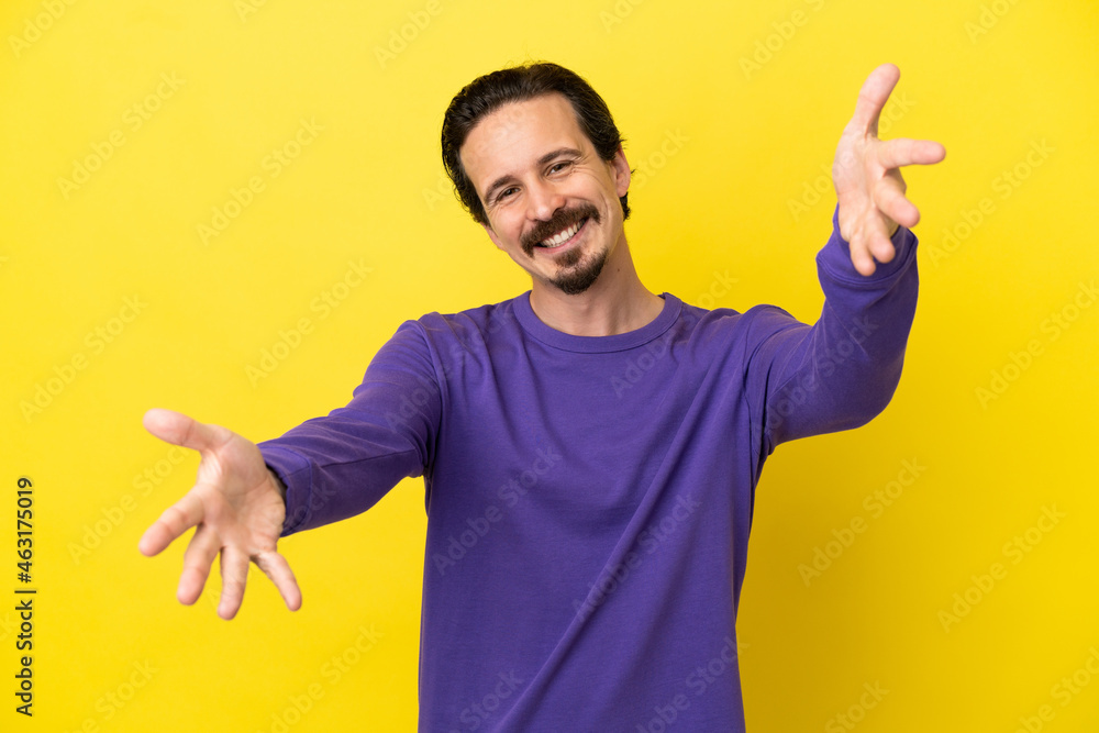 Young caucasian man isolated on yellow background presenting and inviting to come with hand Young caucasian man isolated on yellow background presenting and inviting to come with hand