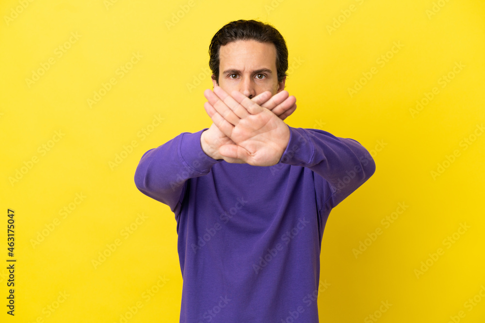 Young caucasian man isolated on yellow background making stop gesture with her hand to stop an act Young caucasian man isolated on yellow background making stop gesture with her hand to stop an act