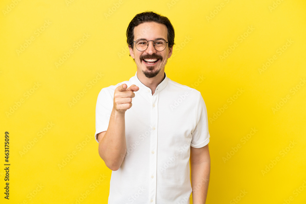 Young caucasian man isolated on yellow background surprised and pointing front Young caucasian man isolated on yellow background surprised and pointing front